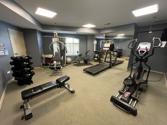 Indoor gym area with exercise equipment including dumbbells, a bench, a treadmill, and an elliptical machine.