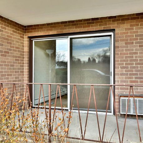 Front view of a brick wall with a large sliding glass door and metal railing.