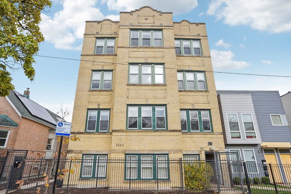 Front view of a multi-story residential building with a yellow brick exterior and green-framed windows.