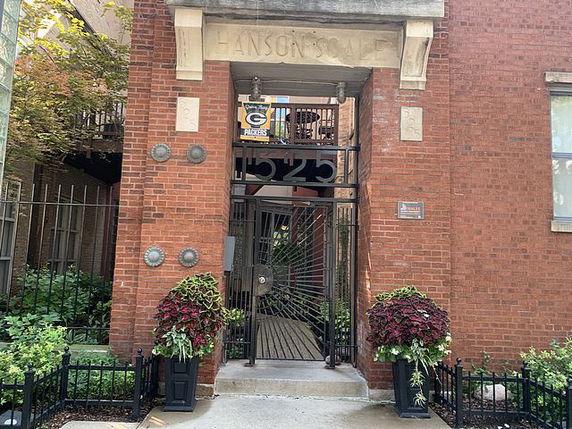Front view of a brick building entrance with ornate metal gate and potted plants.