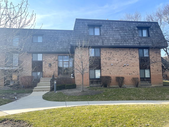 Front view of a two-story brick apartment building with dark shingle roof.