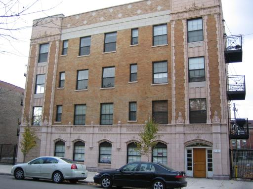 Front view of a four-story apartment building with a brick facade and external fire escapes.