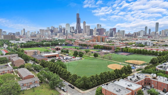 Panoramic view of a city skyline with sports fields and residential buildings in the foreground.