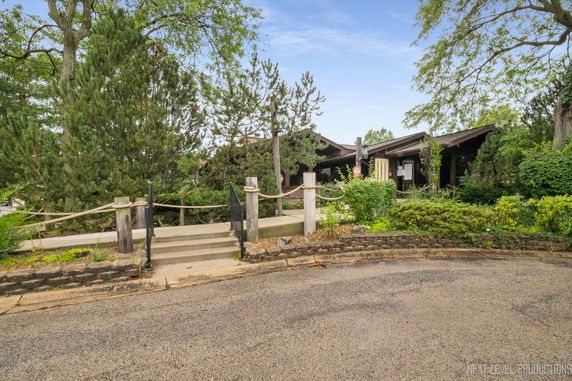 Front view of a single-story house with a sloped roof, surrounded by trees and greenery.