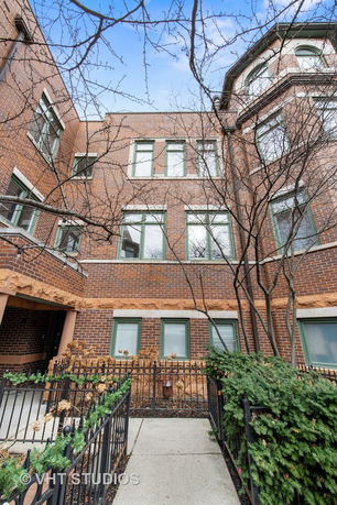Front view of a multi-story brick building with large windows and a small garden path leading to the entrance.
