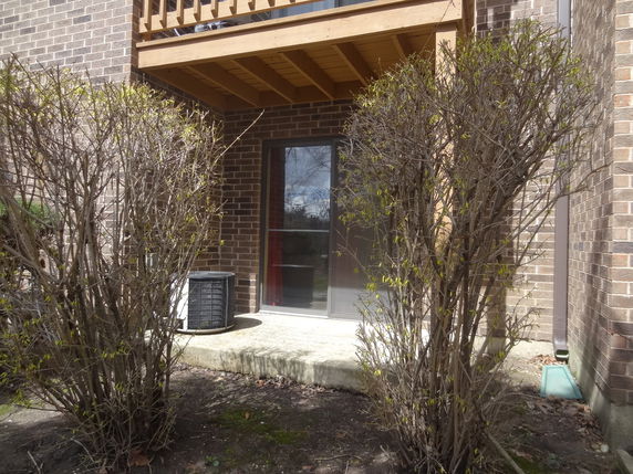 View of a brick building with a wooden balcony and a glass door at ground level.