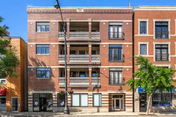 Front view of a multi-story brick building with balconies and storefronts on the ground floor.