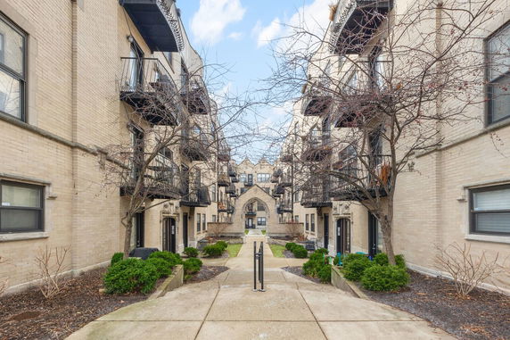 View of a multi-story building complex with balconies and an arched entrance.