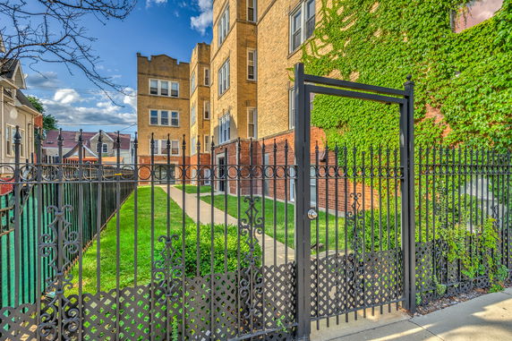Front view of a multi-story brick building with ivy-covered walls and secured by a wrought iron gate.