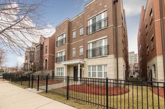 Front view of a multi-story brick building with balconies and a fenced front yard.