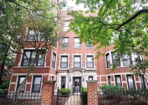 Front view of a multi-story brick apartment building with a gated entrance.