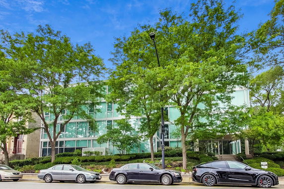 Front view of a modern glass-paneled building with trees and parked cars in front.