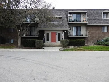 Front view of a two-story residential building with balconies and a red front door.