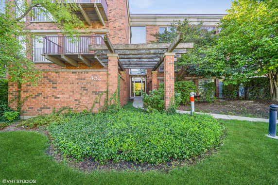 Front view of a brick building with a wooden pergola entrance.