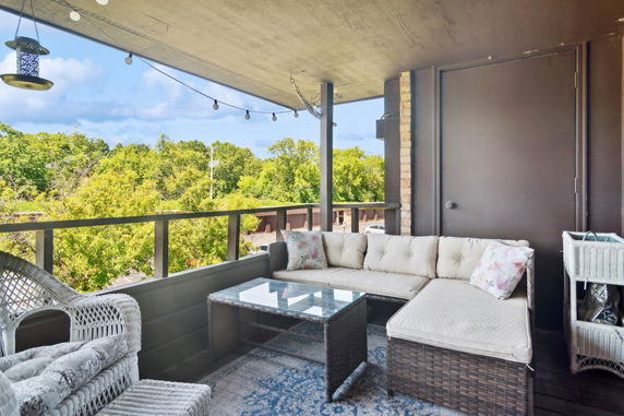 Balcony with outdoor seating, overlooking a green area with trees.