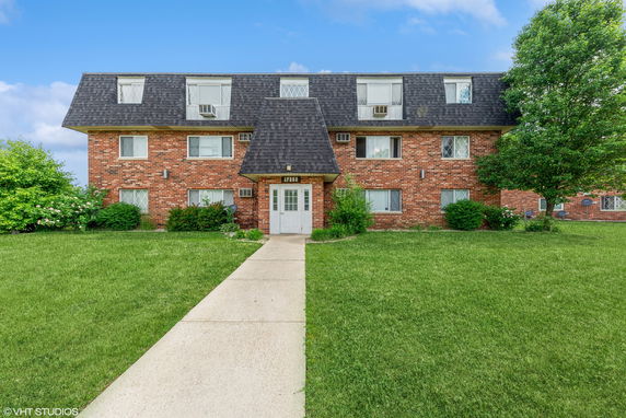 Front view of a brick apartment building with a sloped roof and central entrance.