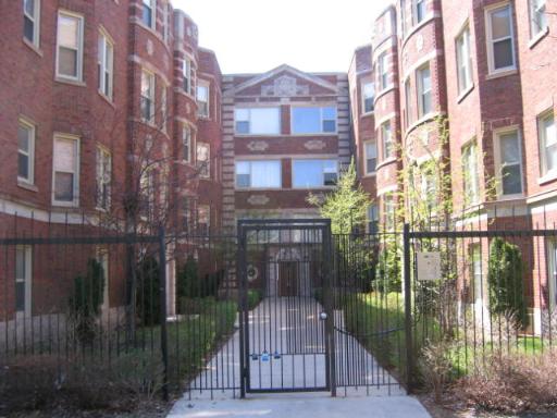Front view of a multi-story brick apartment building with gated entrance.