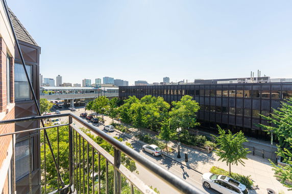 Panoramic view of a city street from a balcony, showing buildings and trees.