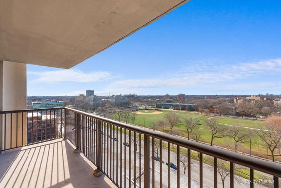 View from a balcony overlooking a park and cityscape under a clear blue sky.