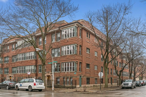 Front view of a multi-story brick apartment building on a city street corner.