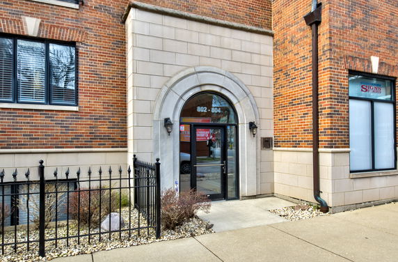 Front view of a brick building entrance with an arched glass door and decorative stonework.