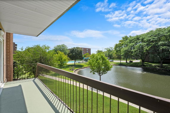 View from a balcony overlooking a pond, trees, and a swimming pool in the distance.