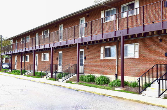Front view of a two-story brick building with multiple entrances and a railing on the upper level.