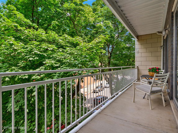 Balcony view with chairs and a table, overlooking trees and part of the street.