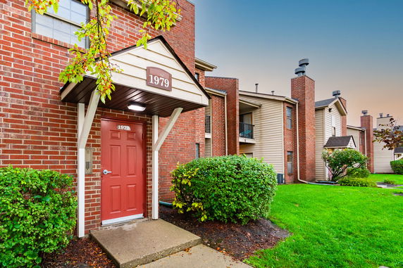 Front view of a multi-story brick apartment building with a red door and greenery.