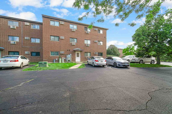 Front view of a three-story brick apartment building with parking spaces.