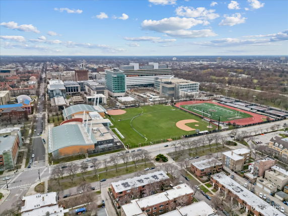 Aerial view of a cityscape with athletic fields, buildings, roads, and surrounding areas.