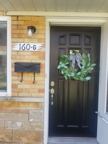 Front view of a house entrance with a black door and a decorative wreath.