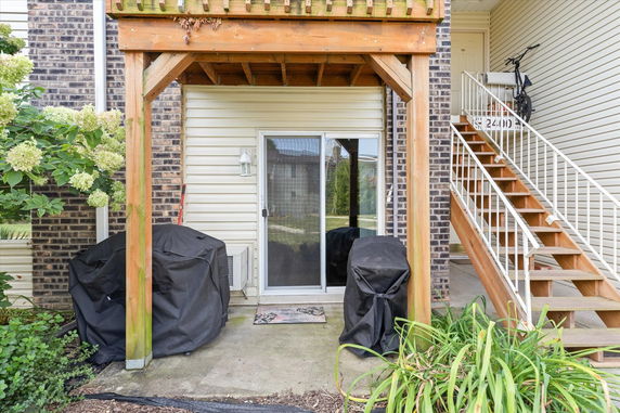 Rear view of a house with a sliding glass door, wooden pergola, and external staircase.