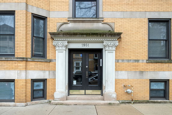 Front view of a multi-story brick building with decorative entrance and black framed windows.