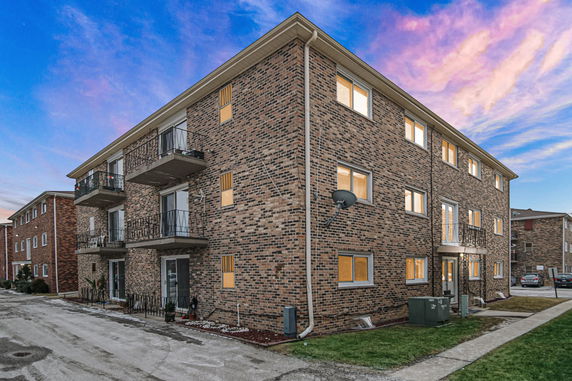Front view of a three-story brick apartment building with balconies.