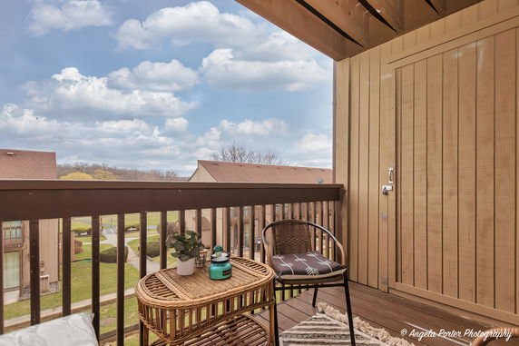 View from a balcony with a chair and table overlooking rooftops and open sky.