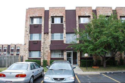 Front view of a multi-story brick apartment building with parked cars.