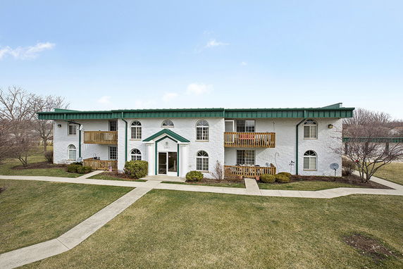 Front view of a two-story apartment building with green roof accents and balconies.
