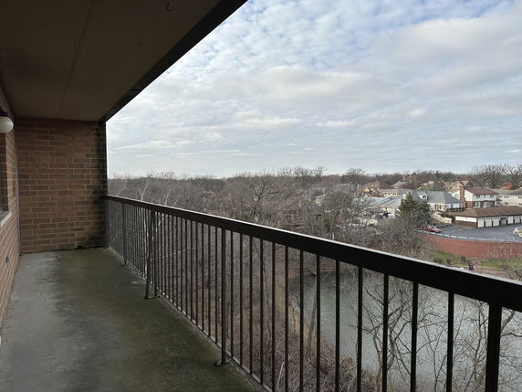View of surrounding areas from an upper-level balcony with trees and houses in the distance.