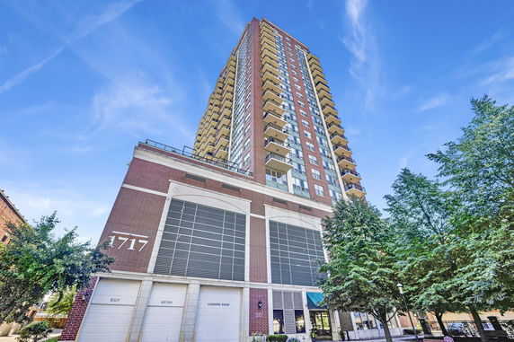 Front view of a tall residential building with multiple balconies and a brick facade.