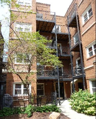 Front view of a multi-story brick apartment building with metal balconies.