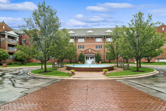 Front view of a brick apartment building with a circular driveway and central fountain.