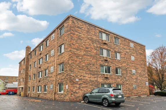 Front view of a four-story brick apartment building with parking area.