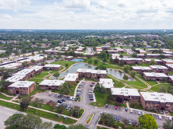 Wide aerial view of a residential area with multiple buildings, roads, and greenery.