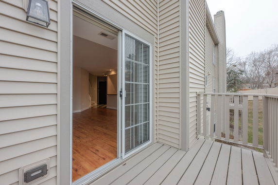Exterior view of a house with beige siding and a small balcony leading to a sliding glass door.