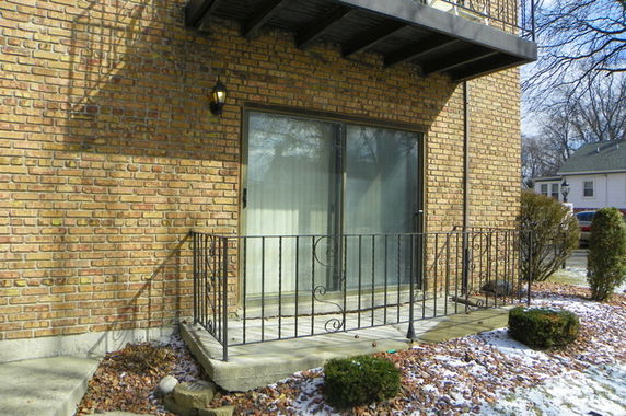 Front view of a brick house with a small balcony and metal railing.