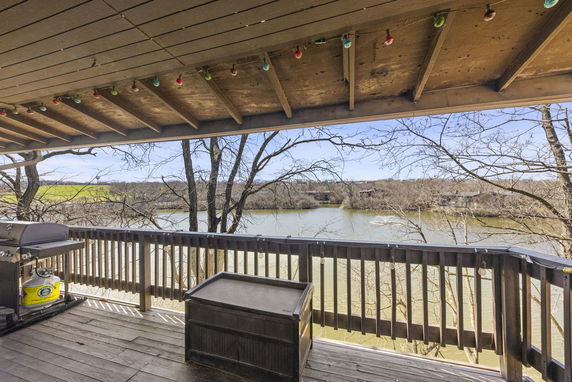 Deck view with wooden railing overlooking a river and surrounding landscape.