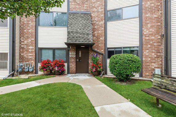 Front view of a building with brick and siding exterior, entrance door, windows, and decorative planters.