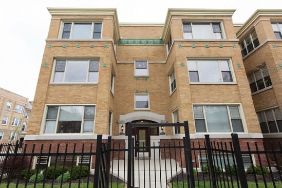 Front view of a multi-story brick building with large windows and a gated entrance.