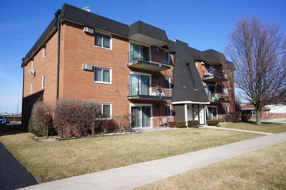 Front view of a multi-story brick apartment building with balconies.